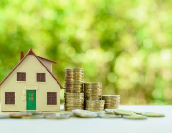 Property investment / reverse mortgage, financial concept : Small home or house model with green door and stacks of rising coins, depicts saving money to buy a new residential asset, human basic needs